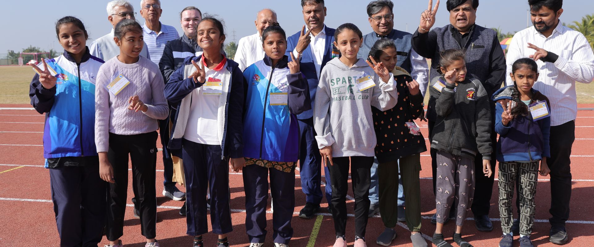 Smiling girl athletes and officials on the running track at the Special Khel Mahakumbh 2025 state-level competition, Porbandar